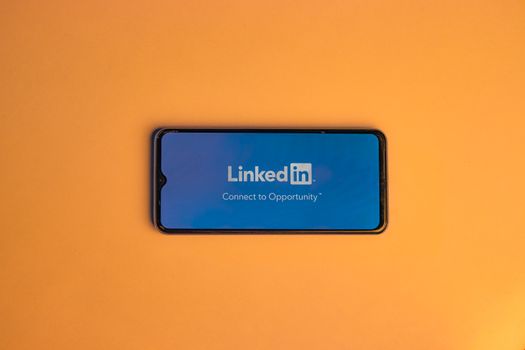 Smartphone showing LinkedIn login on vibrant orange background, symbolizing connectivity.